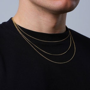 Könnte beinhalten: Ein Mann trägt ein schwarzes T-Shirt mit drei goldenen Ketten.