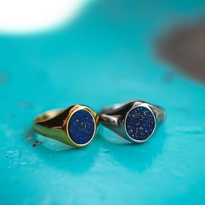 May include: Two signet rings with blue gemstone inlays. One ring is gold and the other is silver.