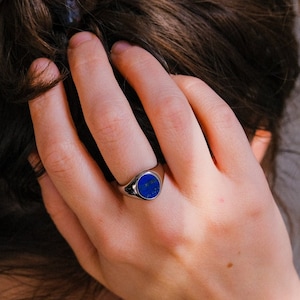 Op de afbeelding: Een zilveren zegelring met een blauwe edelsteen. De ring wordt gedragen aan de wijsvinger van een hand.