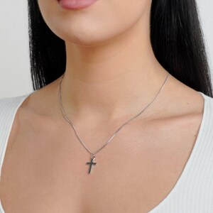May include: A silver chain necklace with a small silver cross pendant. The necklace is worn by a person with long black hair.
