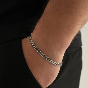 May include: A silver chain bracelet with a curb link design. The bracelet is worn on a person's wrist.