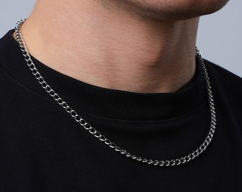 May include: A silver chain necklace on a person wearing a black t-shirt.