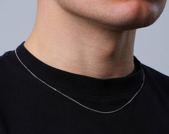 May include: A silver chain necklace worn by a person with a black shirt.
