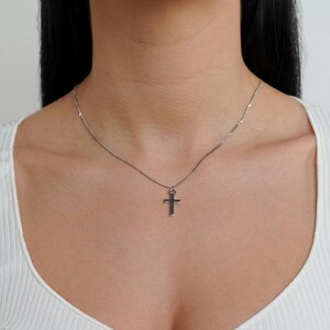 May include: A silver chain necklace with a small silver cross pendant.