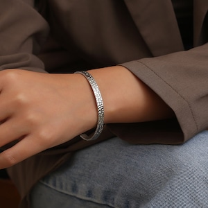 May include: A silver textured bangle bracelet. The bracelet is open and has a hammered finish.