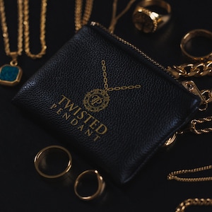 May include: A black leather pouch with a gold zipper and the words "Twisted Pendant" printed on the front. The pouch is surrounded by gold chains and rings.