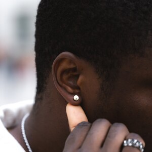 May include: A close-up of a person's ear with a small, round, silver earring. The person has short, black hair and dark skin.
