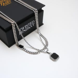 May include: A silver necklace with two chains, one rope-style and one curb-style, featuring a black octagonal pendant. The necklace is displayed on a black box with the text "TWISTED PENDANT".