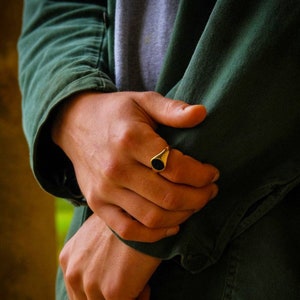 A man wearing a An 18K Gold Signet Ring with a Black Onyx Gemstone in the centre. The Ring is worn on the index finger.