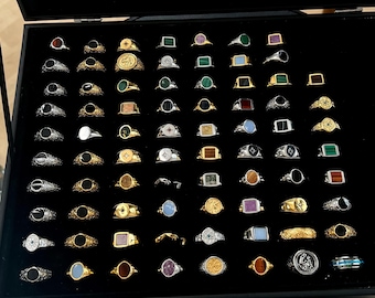 May include: A display case filled with various rings. The rings feature a variety of designs, including gold bands, silver bands, and rings with colorful gemstones. The rings are arranged on a black velvet surface.
