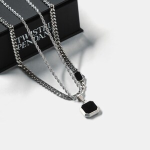 May include: Silver-toned layered necklace set. The set includes a curb chain, a rope chain, and a pendant with a black, octagonal stone. The necklace is displayed on a black box with the text "TWISTED PENDANT".