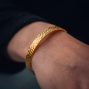 Puede incluir: Un brazalete de oro martillado con una superficie texturizada.