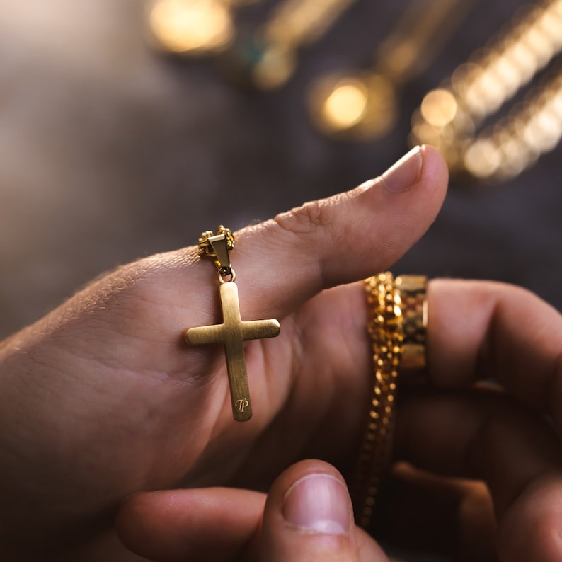May include: A gold chain necklace with a gold cross pendant. The cross has a small inscription on the back.