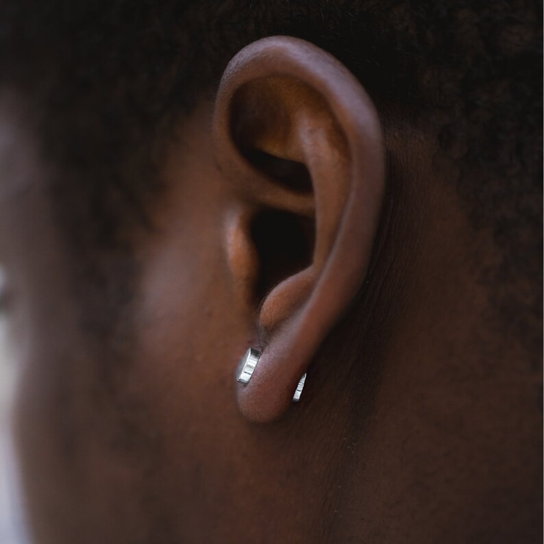 May include: A close-up of a person's ear with two small silver hoop earrings.
