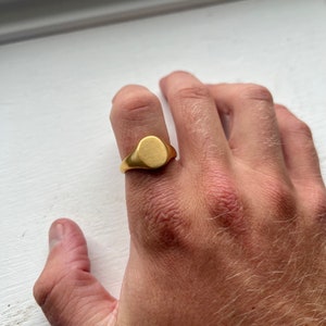 May include: A gold signet ring with a smooth, oval-shaped top.