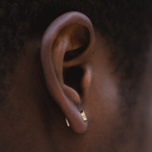 May include: A close-up of a person's ear with two small gold hoop earrings.