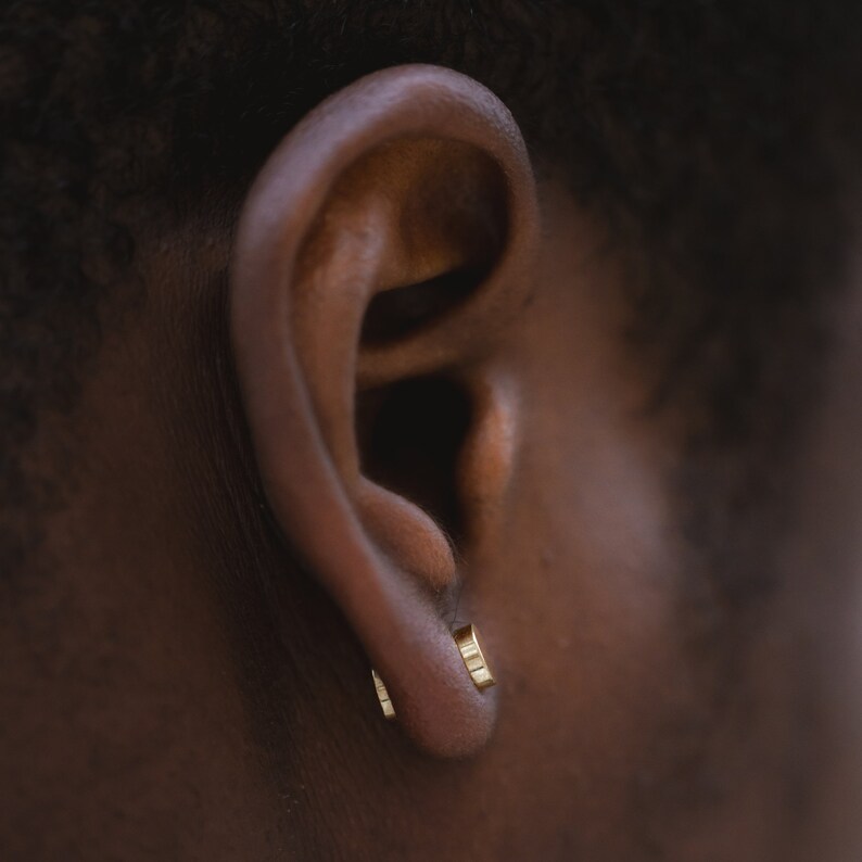 May include: A close-up of a person's ear with two small gold hoop earrings.