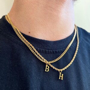 May include: Two gold chains with initial pendants, one chain is a rope chain and the other is a curb chain. The pendants are the letters 'B' and 'H'.