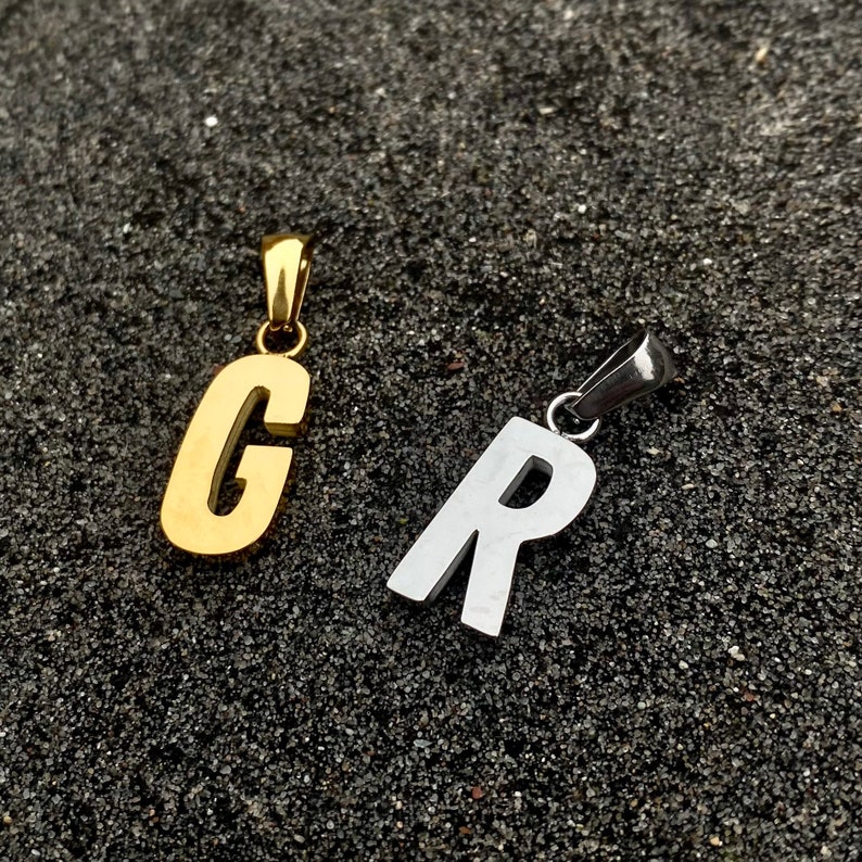 May include: Two metal letter pendants, one gold and one silver. The gold pendant is the letter "C" and the silver pendant is the letter "R".
