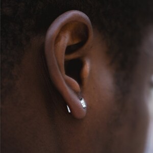 May include: A close-up of a person's ear with a small silver hoop earring in each lobe.