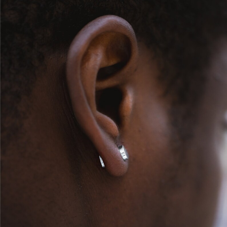 May include: A close-up of a person's ear with a small silver hoop earring in each lobe.