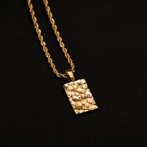 Könnte beinhalten: Eine goldene Kettenkette mit einem strukturierten rechteckigen Anhänger.