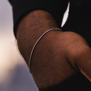 Puede incluir: Un brazalete de cadena de plata en la muñeca de una persona.