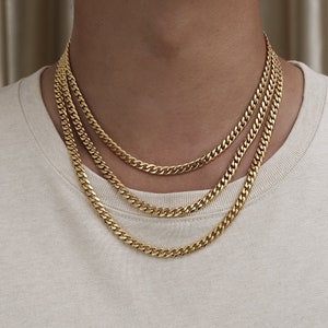 May include: Three gold chain necklaces layered on a person's neck. The chains are all the same style, but different lengths.