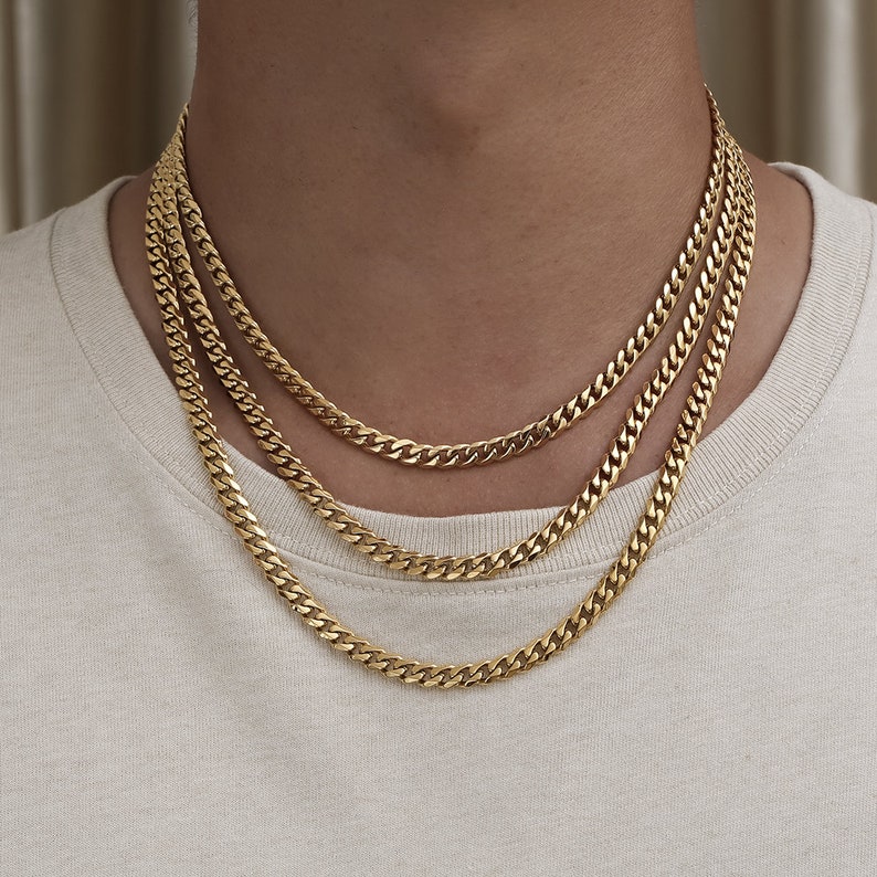 May include: Three gold chain necklaces layered on a person's neck. The chains are all the same style, but different lengths.
