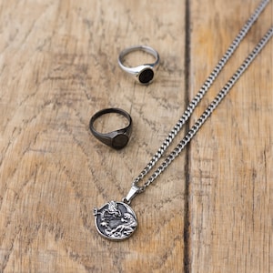 May include: A silver chain necklace with a black dragon pendant. The pendant is round and features a detailed design. The necklace is also paired with two black signet rings.