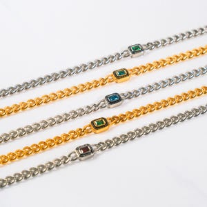 May include: Five silver and gold-toned chain bracelets with square-cut, colorful gemstones. The gemstones are green, blue, and red. The bracelets are arranged diagonally against a white background.