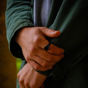 A man wearing a All Black Signet Ring with an Onyx Gemstone in the centre. The Ring is worn on the index finger.
