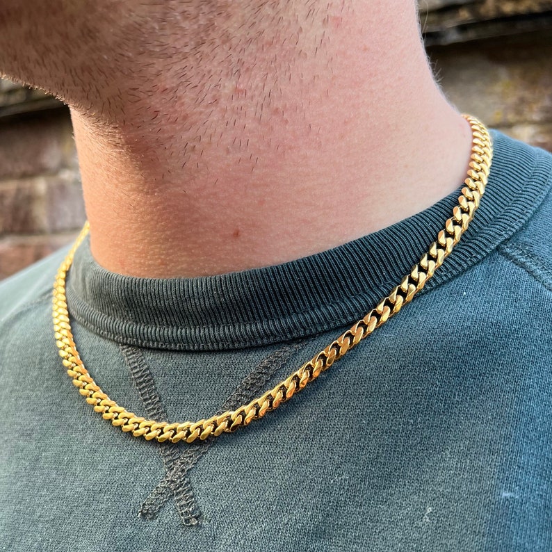 May include: A gold chain necklace with a curb link style. The chain is worn by a person, but the person's face is not visible.