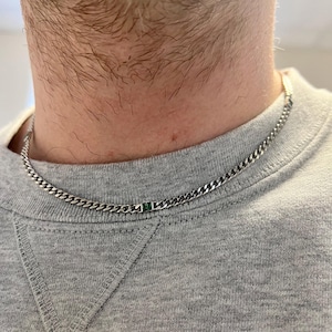 May include: A silver chain necklace with a small green gemstone accent.