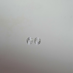 Puede incluir: Dos peque&ntilde;os pendientes de aro plateados. Cada pendiente presenta un dise&ntilde;o de doble banda, creando un efecto de capas. Los pendientes se exhiben sobre una superficie reflectante, realzando su brillo y detalle. El dise&ntilde;o minimalista sugiere simplicidad y elegancia.
