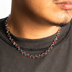 May include: Silver necklace featuring red rectangular stones and star-shaped details. The necklace is set against a dark grey crew neck top. A fashionable piece of jewellery.