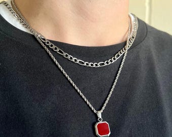 May include: Two silver chains with a red octagon pendant. The chains are layered, with the thicker chain on top. The pendant is a simple geometric shape with a smooth, shiny surface.