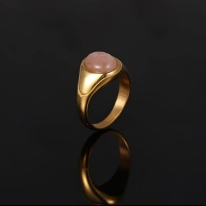 A Silver Signet Ring with a Rose Quartz Pink Gemstone in the middle. The ring is in the middle of a black background.