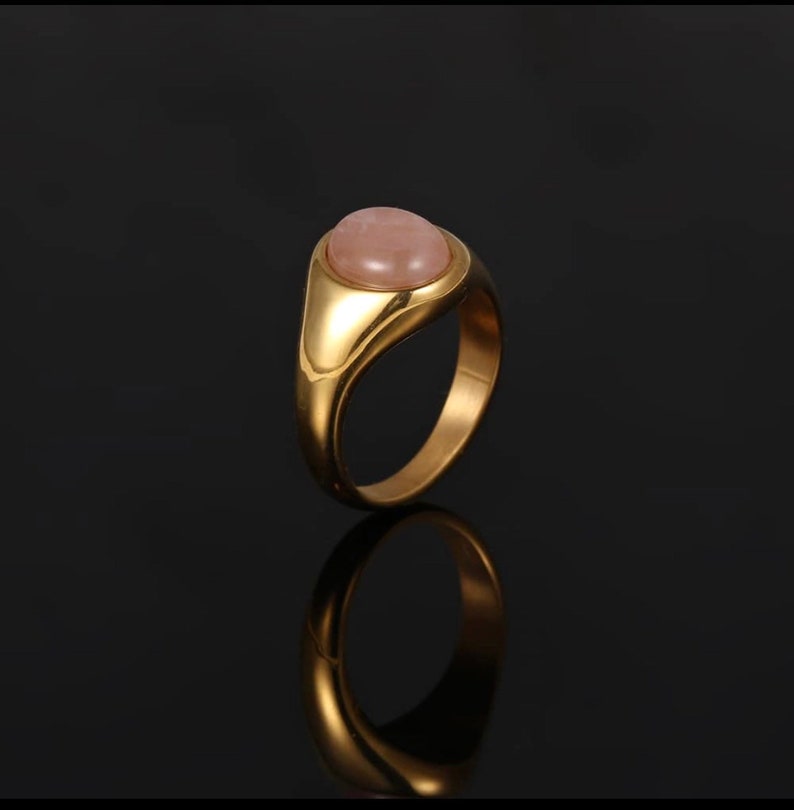 A Silver Signet Ring with a Rose Quartz Pink Gemstone in the middle. The ring is in the middle of a black background.
