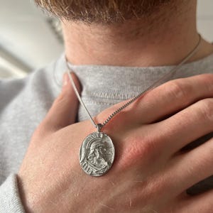 May include: A silver chain necklace with a silver pendant featuring a detailed profile of a person wearing a helmet.