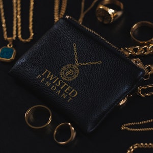 May include: A black leather pouch with the gold text "TWISTED PENDANT" and a gold chain design. Gold necklaces, rings, and chains surround the pouch. The jewelry is displayed on a black surface.
