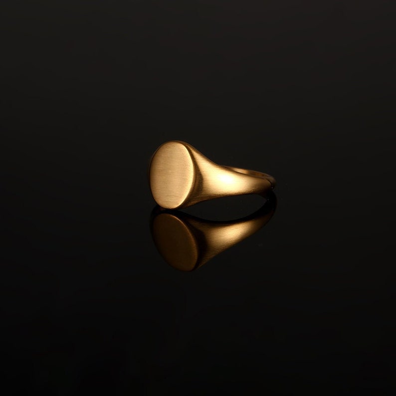 May include: A gold signet ring with a smooth, oval-shaped top.