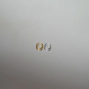 Puede incluir: Se muestran dos anillos, uno dorado y otro plateado. Cada anillo presenta un dise&ntilde;o de doble banda. Los anillos se colocan sobre un fondo reflectante y neutro, destacando su elegante sencillez. Estos anillos son adecuados para el uso diario.