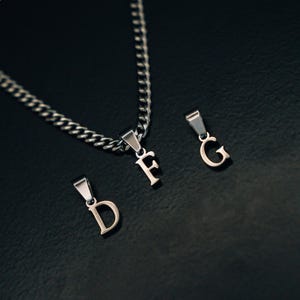 May include: A silver chain necklace with three silver letter pendants. The pendants spell out the letters "D", "F", and "G".