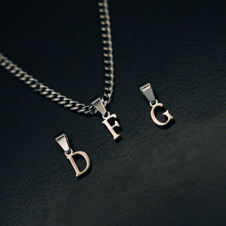 May include: A silver chain necklace with three silver letter pendants. The pendants spell out the letters "D", "F", and "G".
