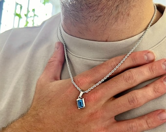 May include: Silver necklace featuring a rectangular, blue gemstone pendant. The chain has a rope design. The pendant is set in a silver frame. The necklace is worn around the neck.