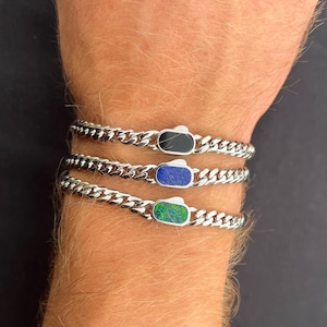 Peut inclure: Trois bracelets à chaîne en argent avec des accents de pierres précieuses rectangulaires. Les pierres précieuses sont noires, bleues et vertes. Les bracelets sont présentés sur le bras d'une personne.