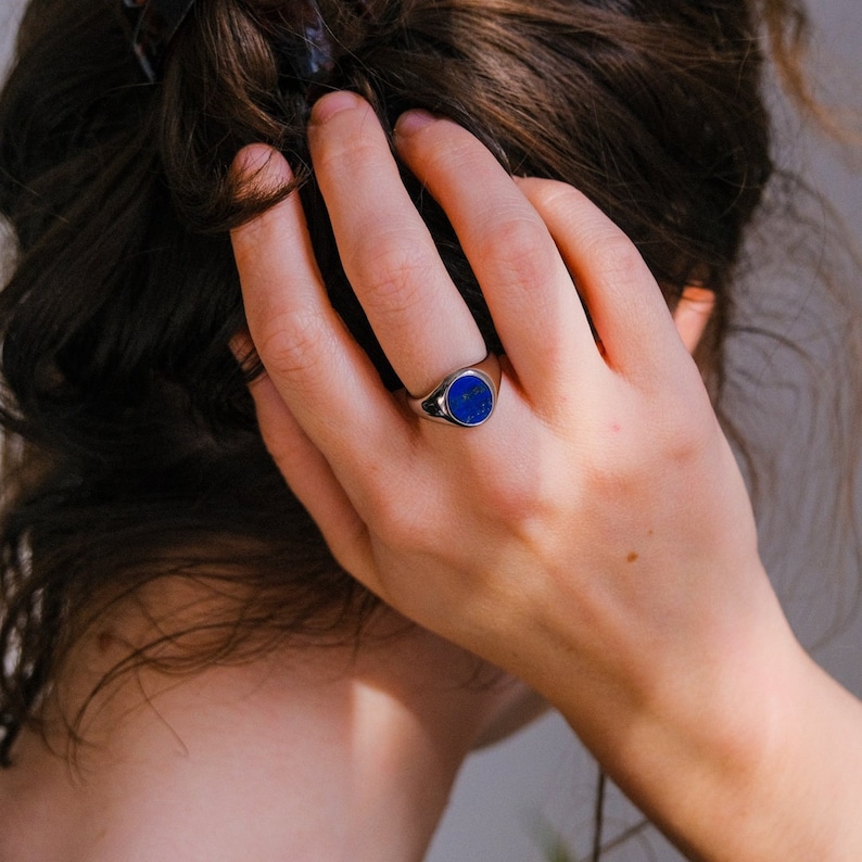 Op de afbeelding: Een zilveren zegelring met een blauwe edelsteen. De ring wordt gedragen aan de wijsvinger van een hand.
