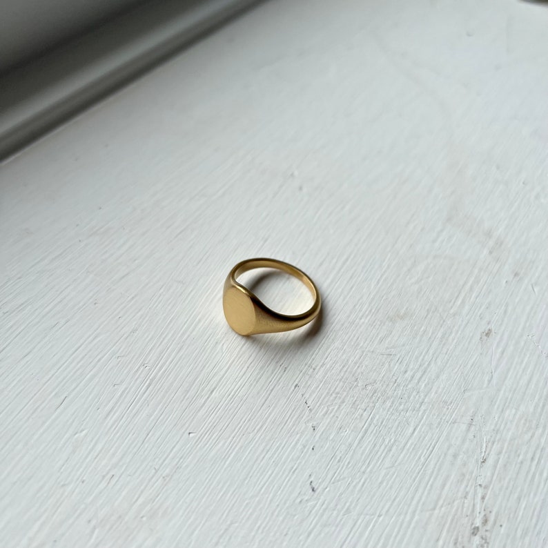 May include: A gold signet ring with a smooth, oval top.