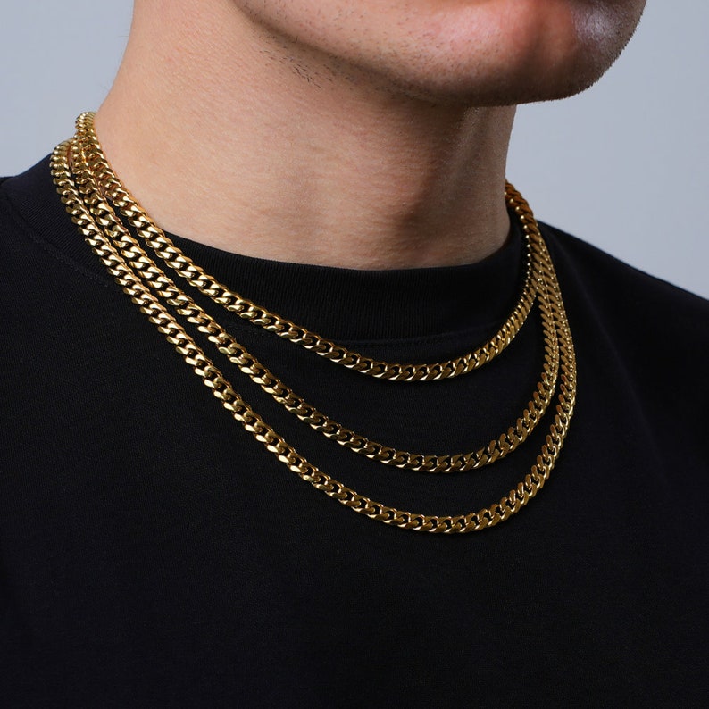 May include: Three gold chain necklaces layered on a person's neck. The chains are all the same style, but different lengths.